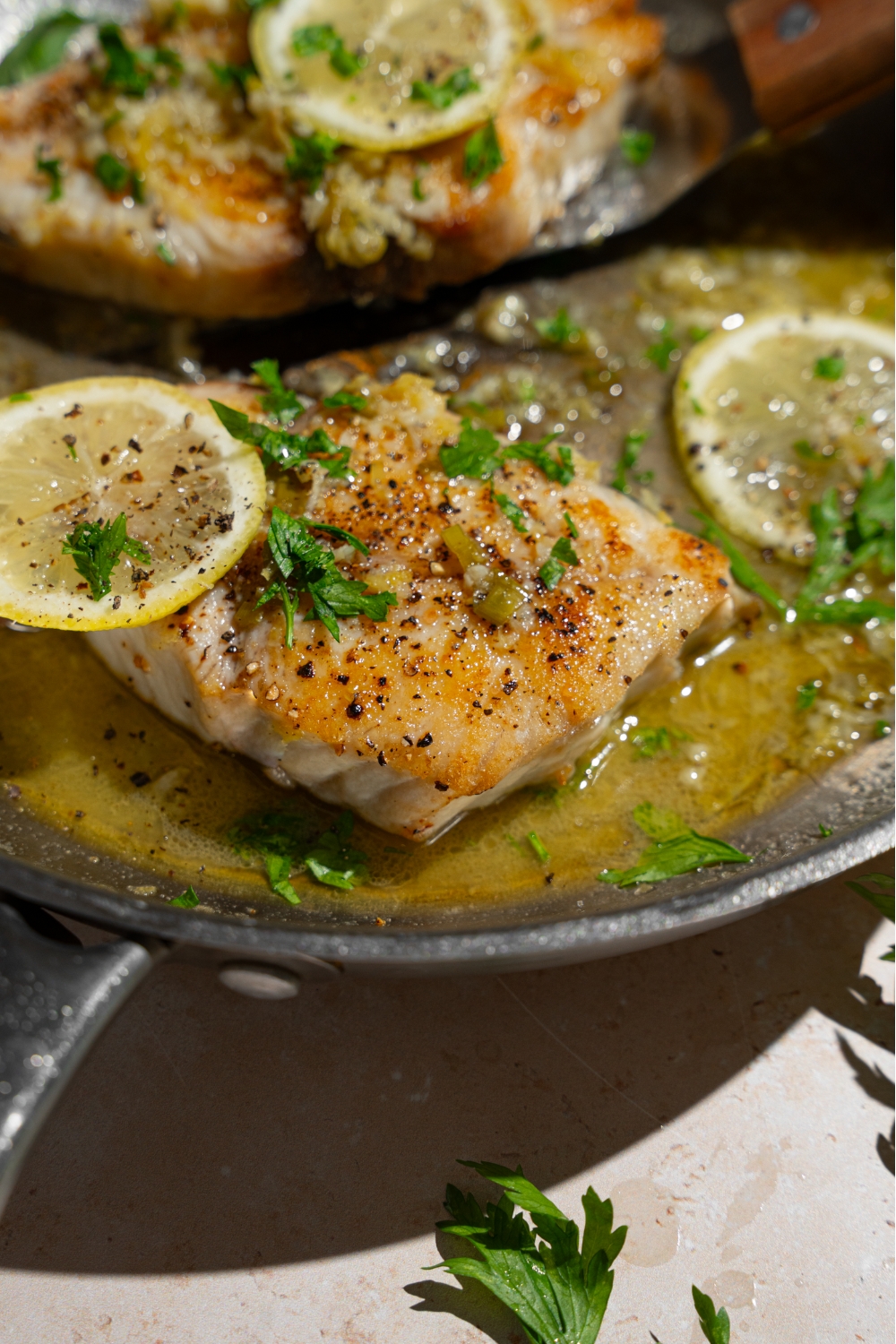A skillet with air fryer swordfish in lemon garlic sauce garnished with fresh parsley and lemon slices.