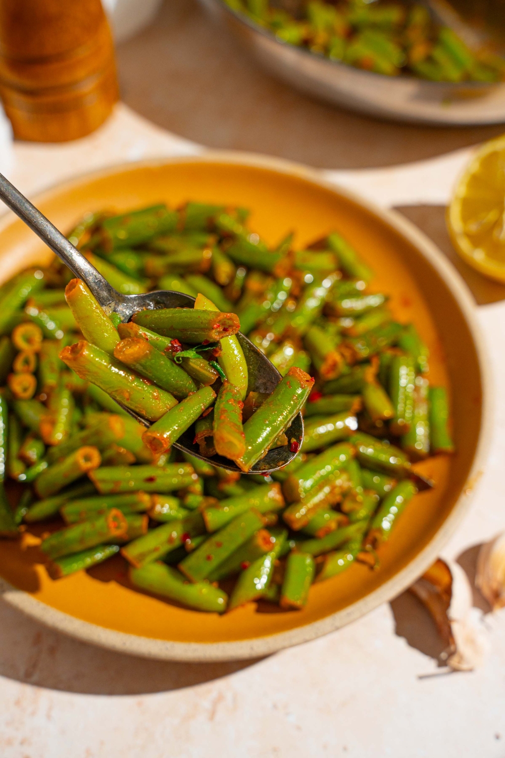 A close up of a spoon with sautéed frozen green beans with a plate of green beans blurred in the background.