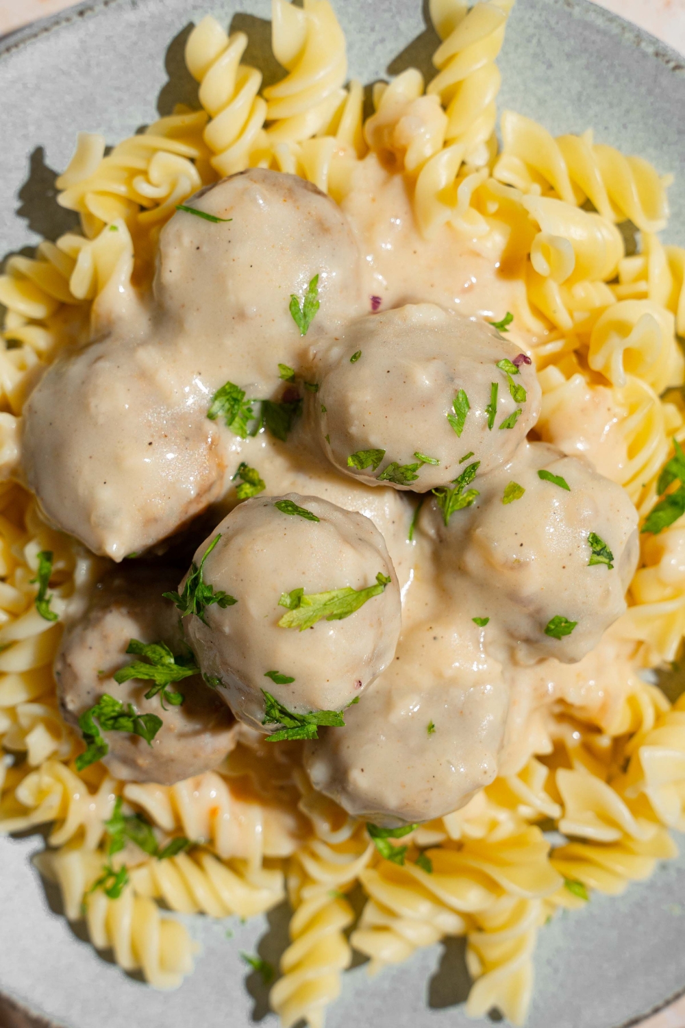 A ceramic plate with pasta topped with Swedish meatballs garnished with fresh parsley.