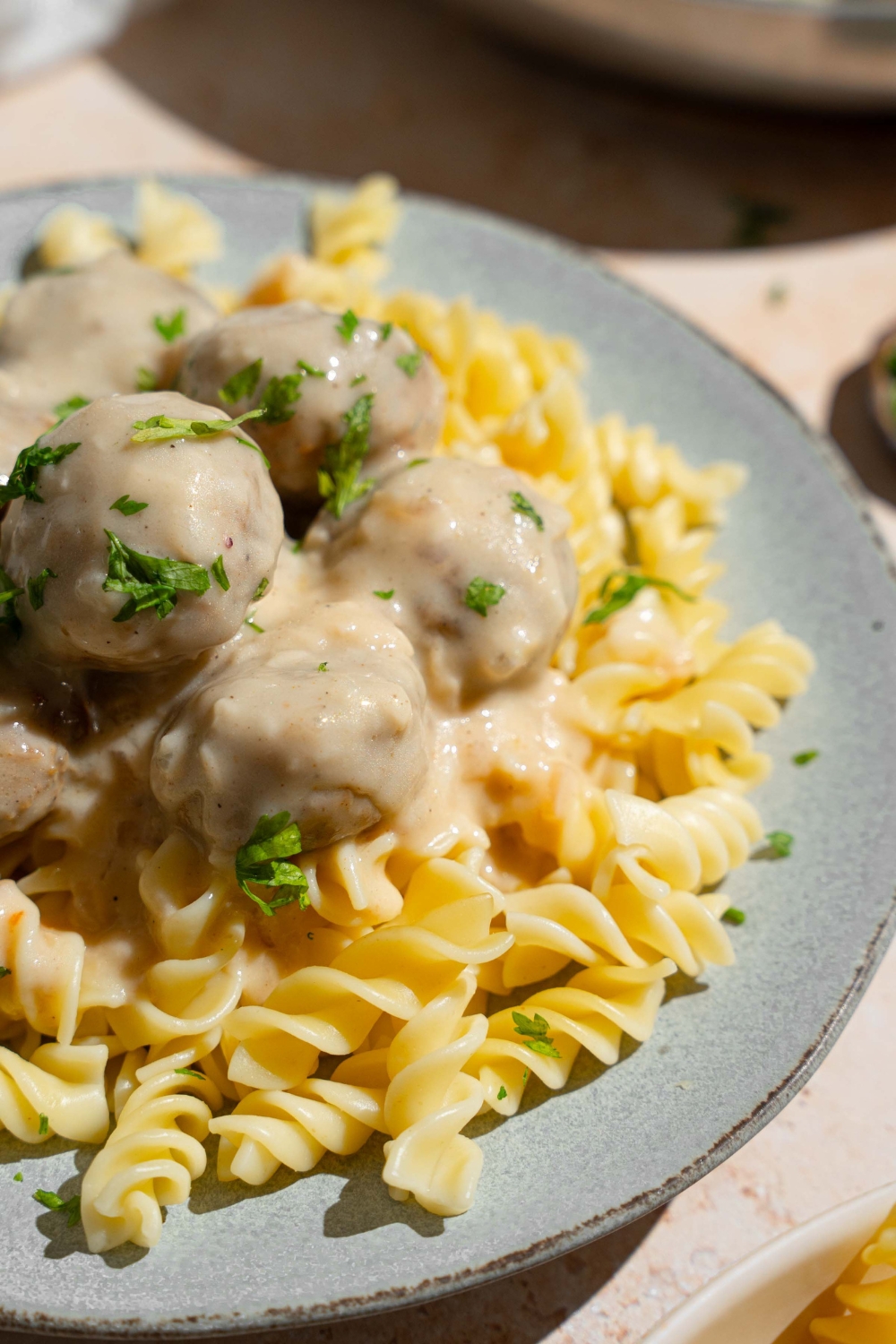 A ceramic plate with pasta topped with Swedish meatballs garnished with fresh parsley. The plate is on a tan counter.