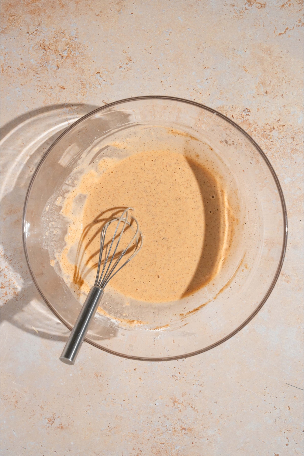 A whisk in a glass bowl of chicken nugget batter.