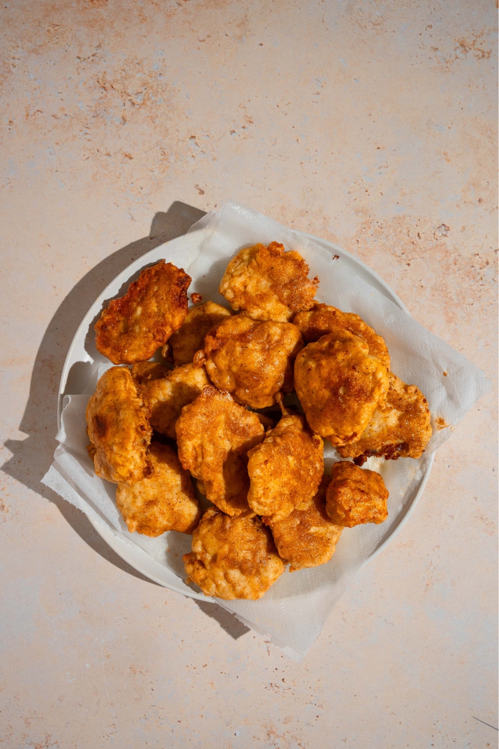 A bunch of fried chicken nuggets on top of the sheet parchment paper on a white plate.