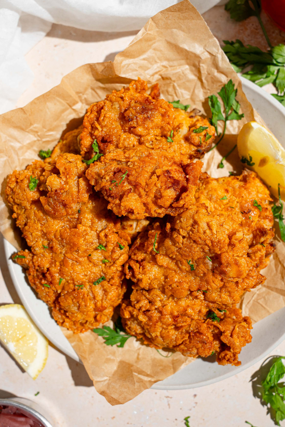 Four fried chicken thighs on top of a sheet of parchment paper that is on a plate.
