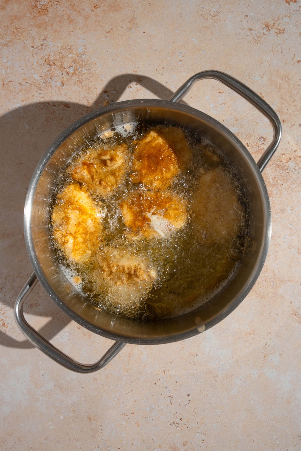 A bunch of chicken nuggets, deep frying in hot oil in a pot.
