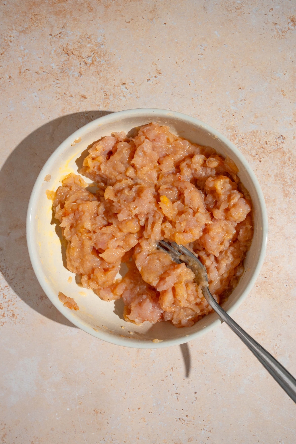 A fork in a white bowl of a ground chicken egg mixture.