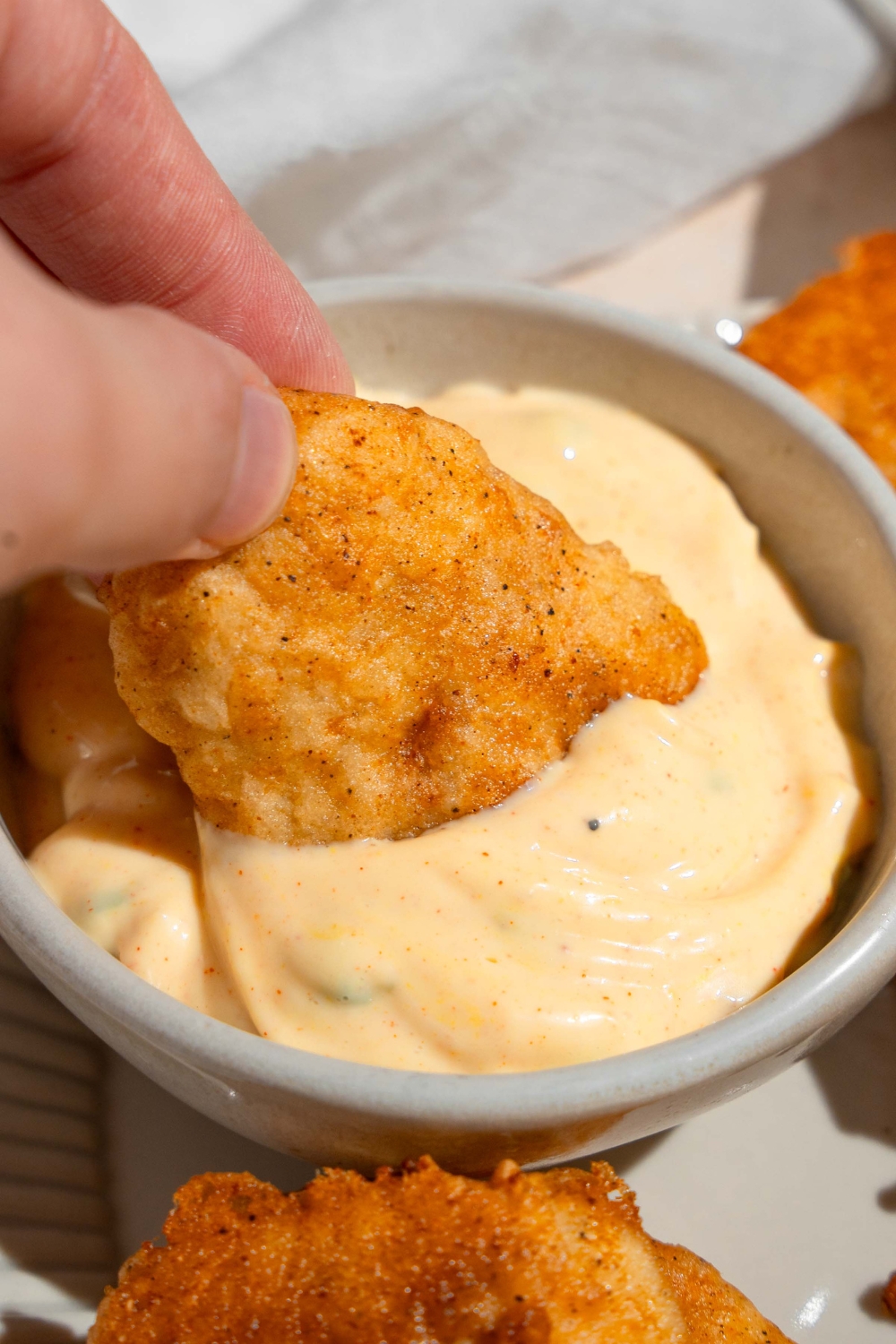 A hand holding a chicken nugget submerged in a cup of sauce.