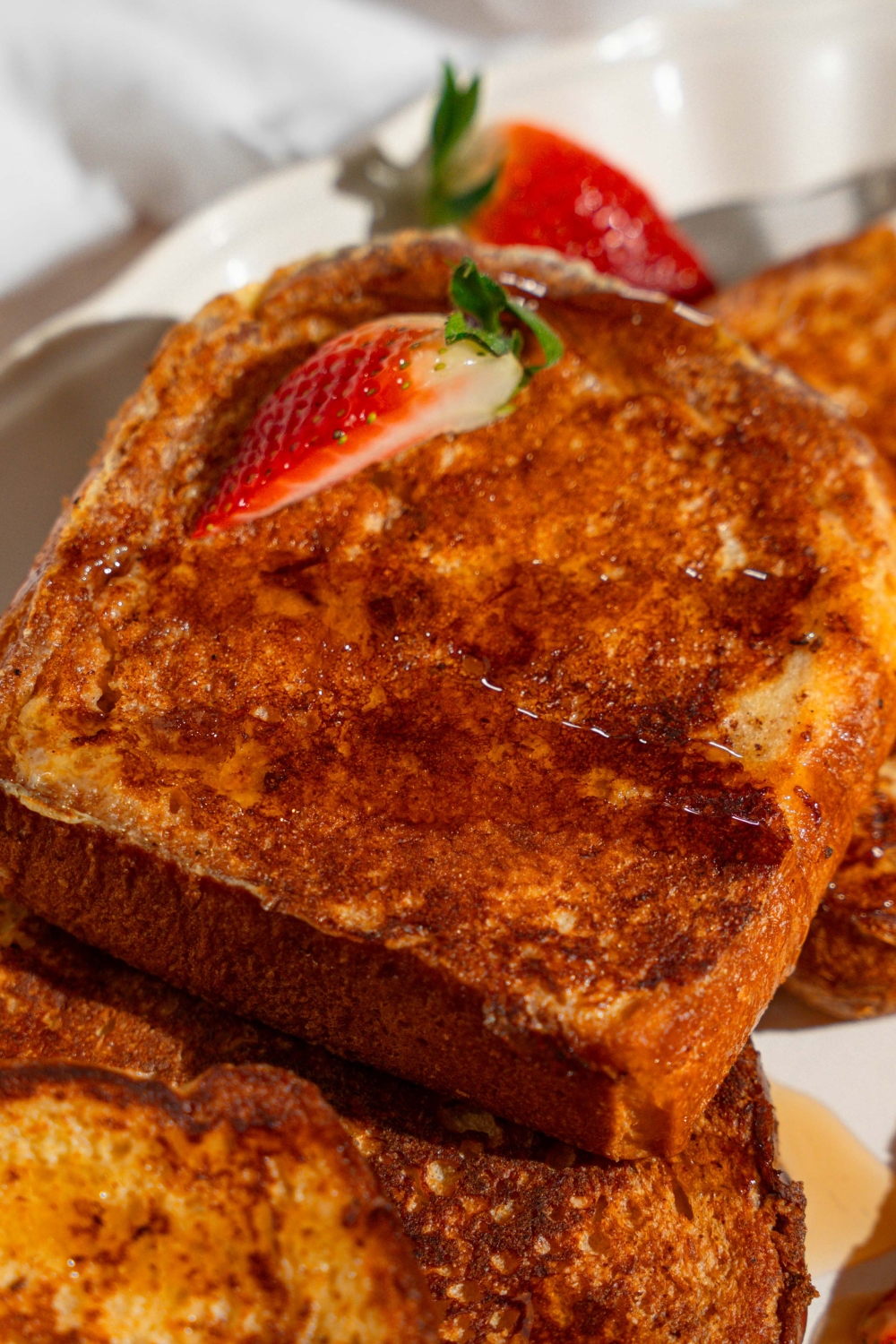 A white platter with slices of French toast drizzled with maple syrup and garnished with sliced strawberries.