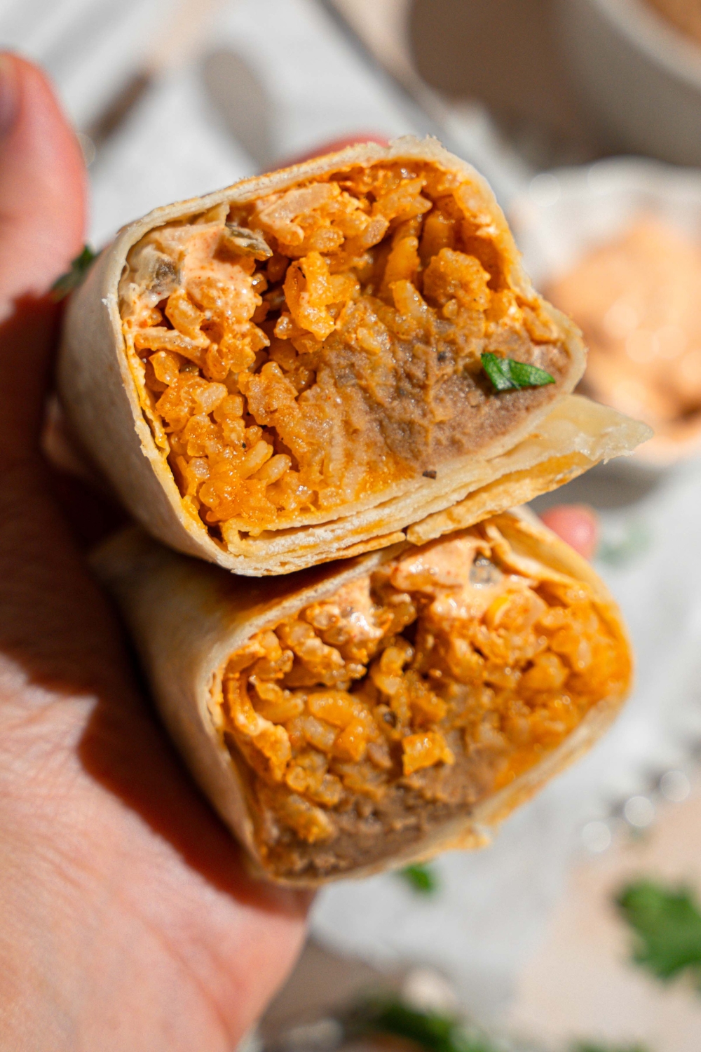 A close up of hand holding a cheesy bean and rice burrito sliced in half.