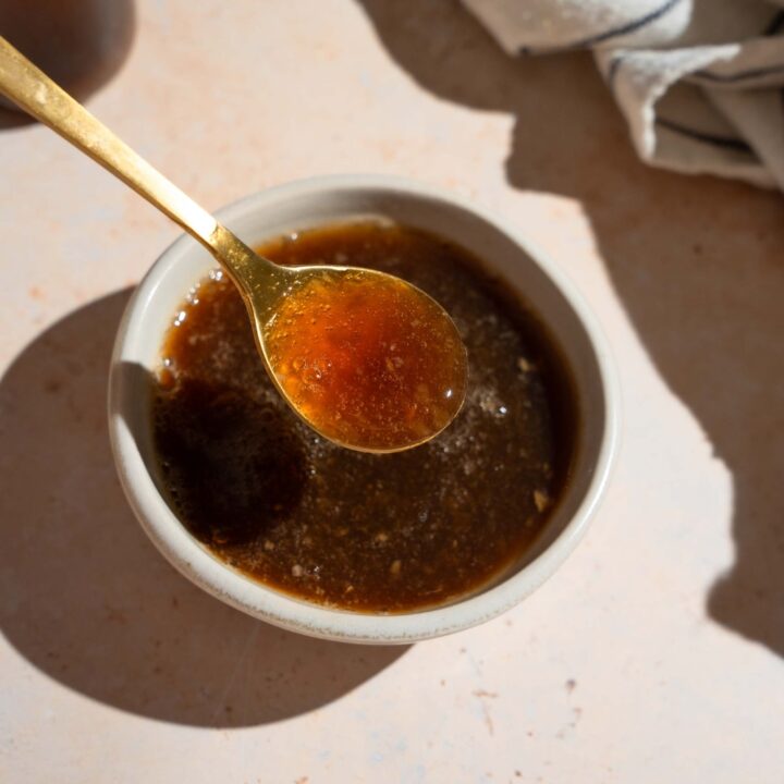 A bowl of oyster sauce with a spoon. The bowl is on a tan counter with a white striped napkin.