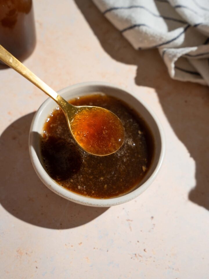 A bowl of oyster sauce with a spoon. The bowl is on a tan counter with a white striped napkin.