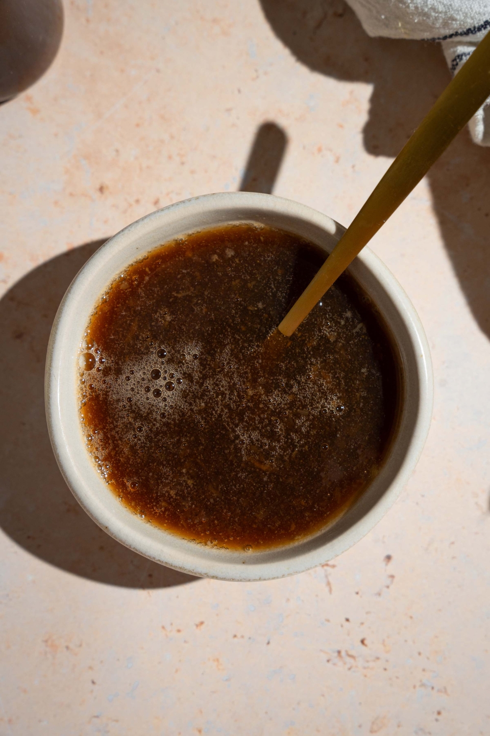A bowl of oyster sauce with a spoon. The bowl is on a tan counter.