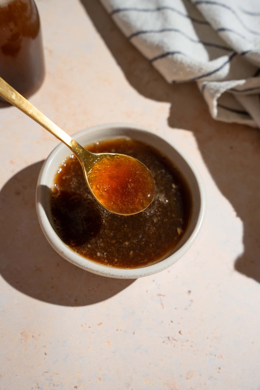 A bowl of oyster sauce with a spoon. The bowl is on a tan counter with a white striped napkin.