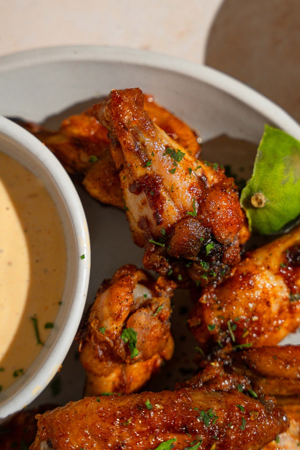 A white plate with copycat Wingstop Louisiana rub wings garnished with fresh parsley, a lime wedge, and small bowl of wing sauce.