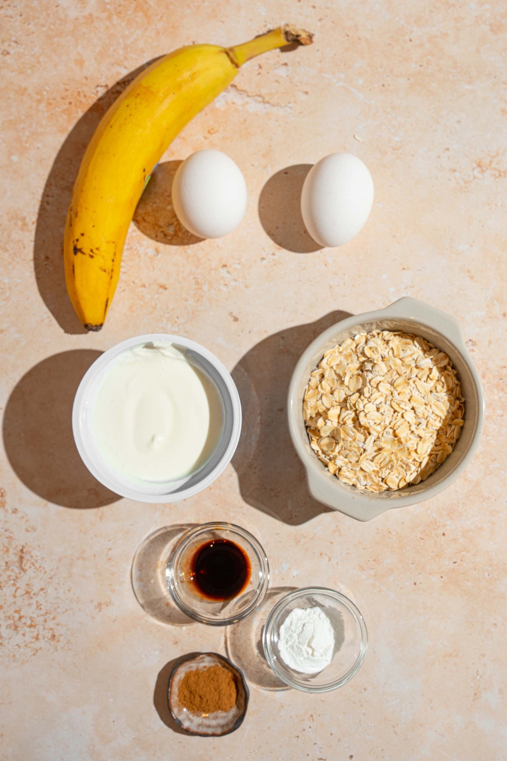 An overhead shot of several bowls in various sizes containing ingredients to make cottage cheese banana pancakes including cottage cheese, oats, banana, eggs, vanilla, cinnamon, and baking powder.