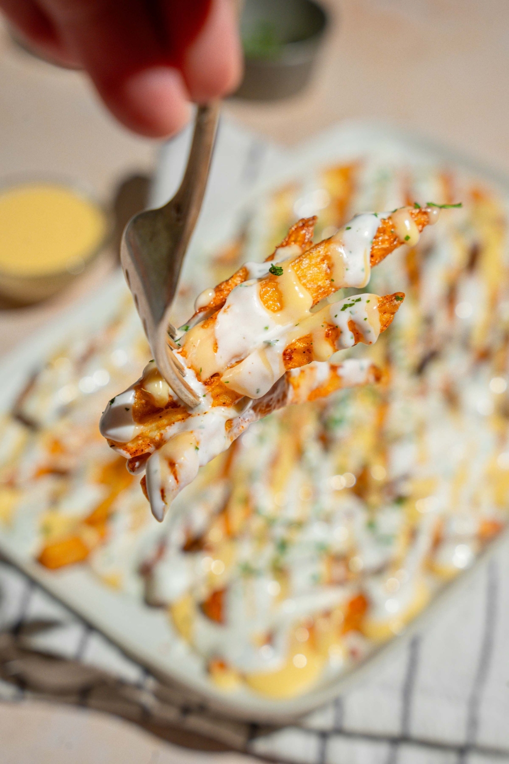 A close up of a fork with a bite of copycat Wingstop Voodoo fries. There is a platter of fries drizzled with cheese and ranch blurred in the background.