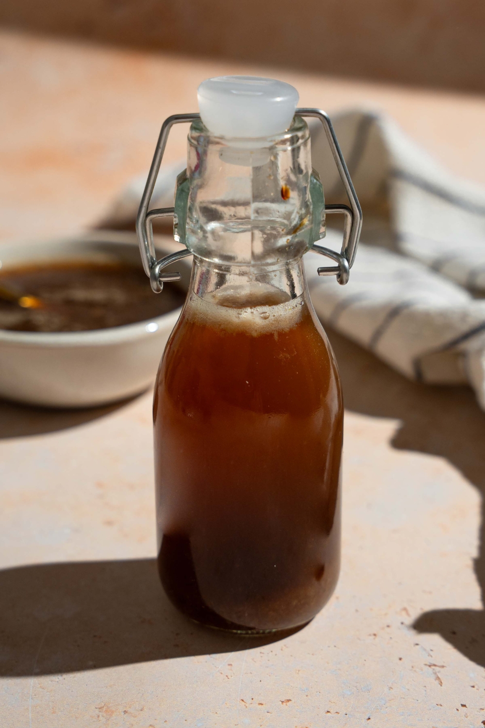 A sealed jar of oyster sauce on a tan counter with a white striped napkin and an additional bowl of sauce.