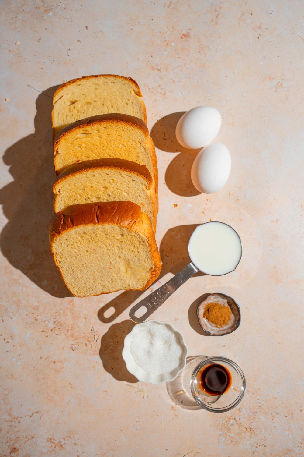 An overhead shot of several ingredients to make French toast for two including brioche bread, milk, eggs, sugar, vanilla, and cinnamon.