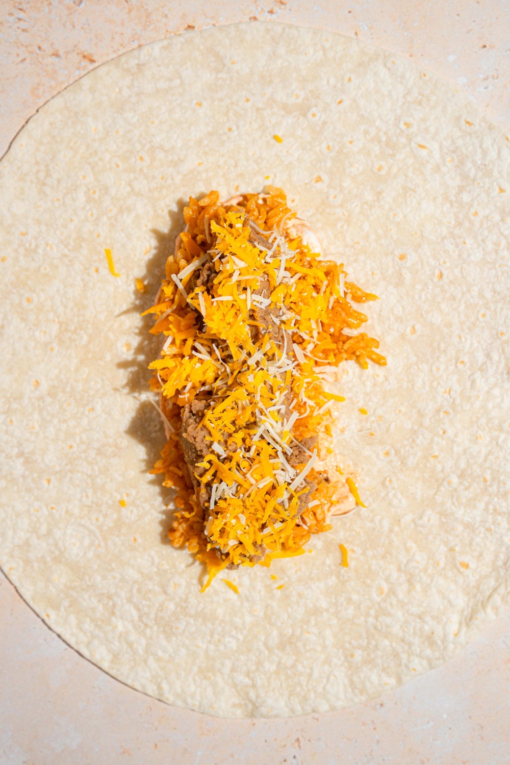 An open cheesy bean and rice burrito on a tan counter.