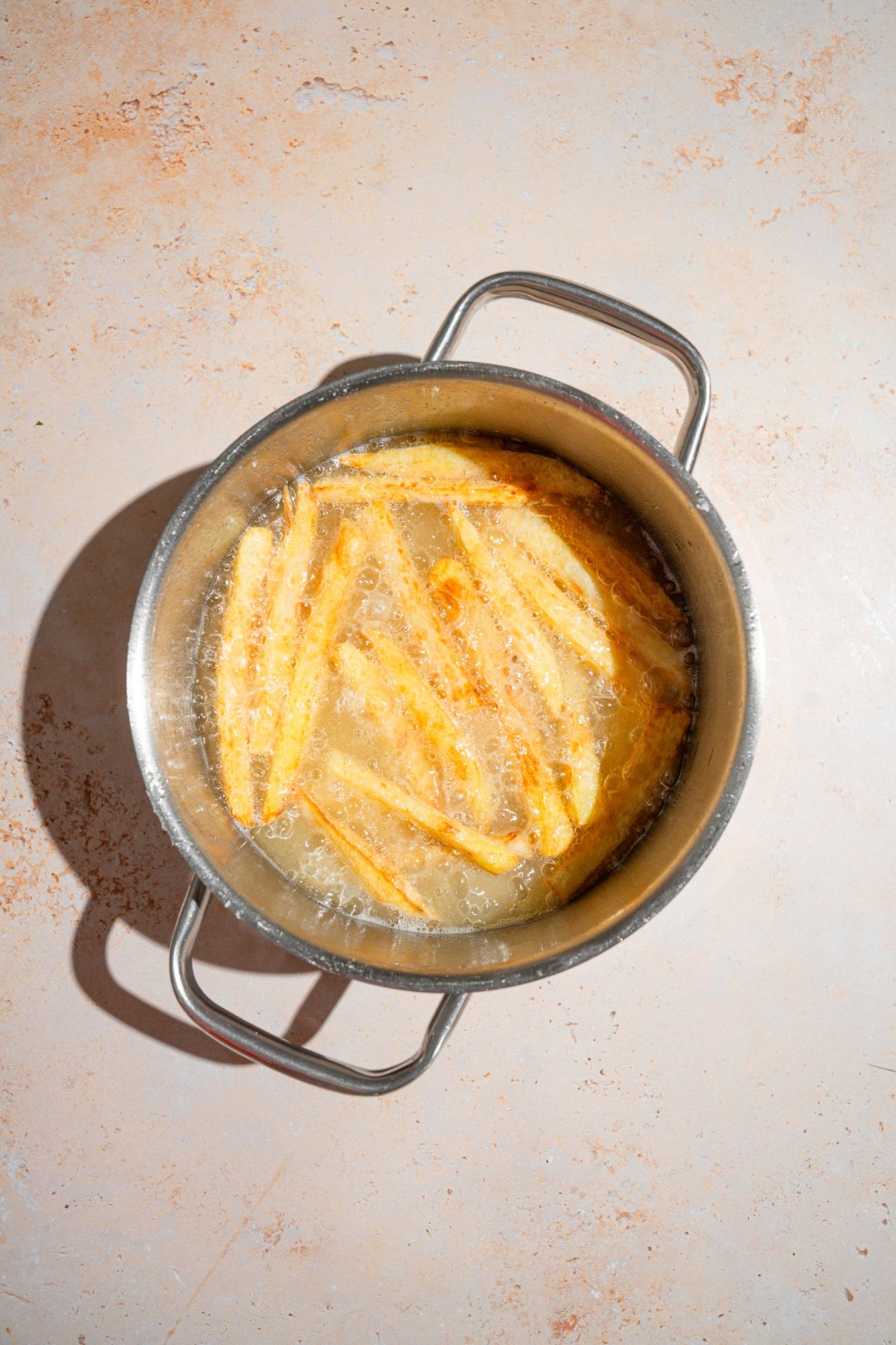 A pot with fries frying in oil. The pot is on a tan counter.