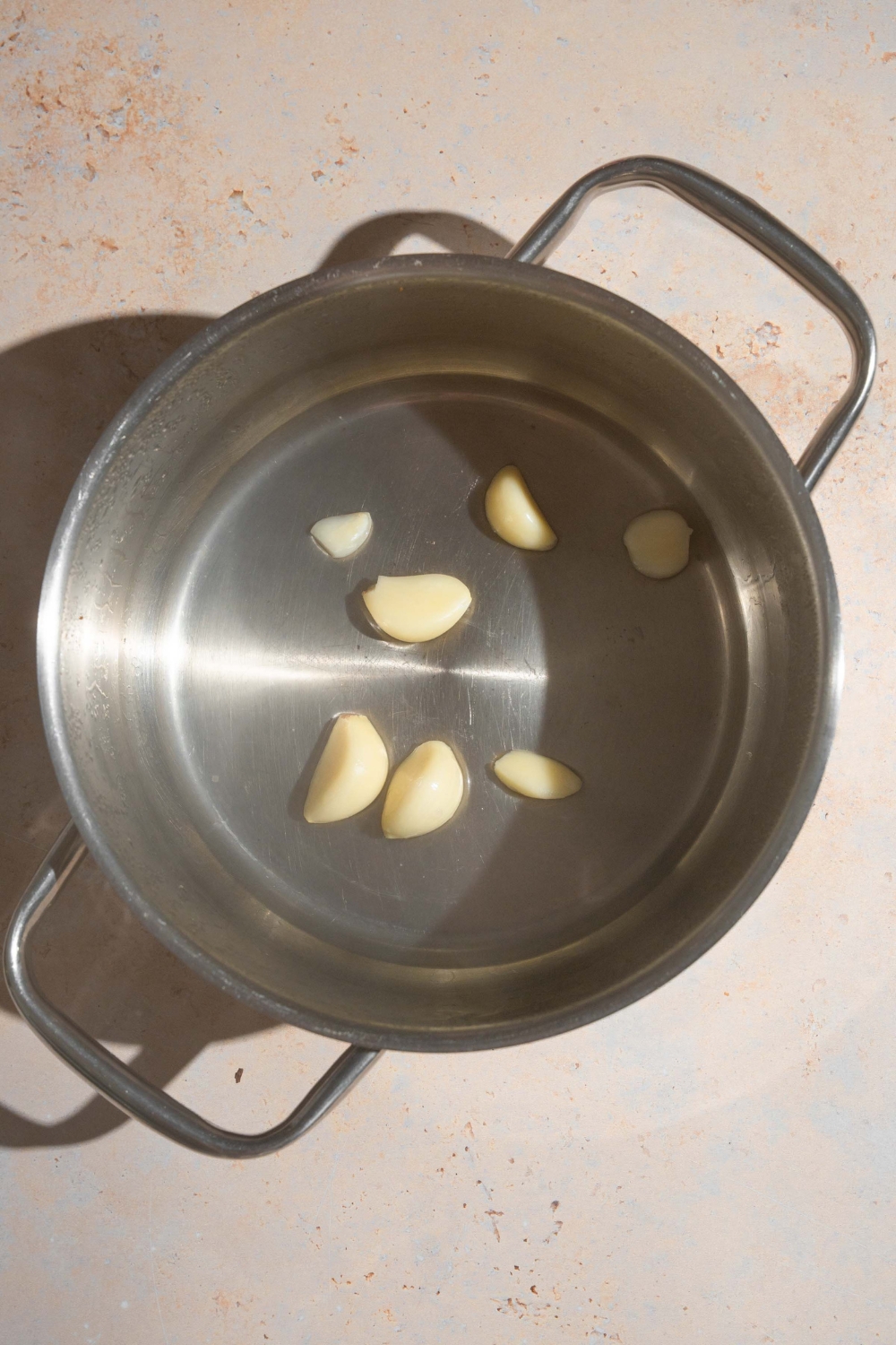 A pot with several garlic cloves in water. The pot is on a tan counter.