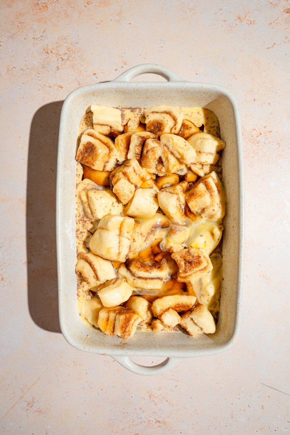 A baking dish with uncooked cinnamon roll french toast soaking in an egg mixture. The dish is on a tan counter.