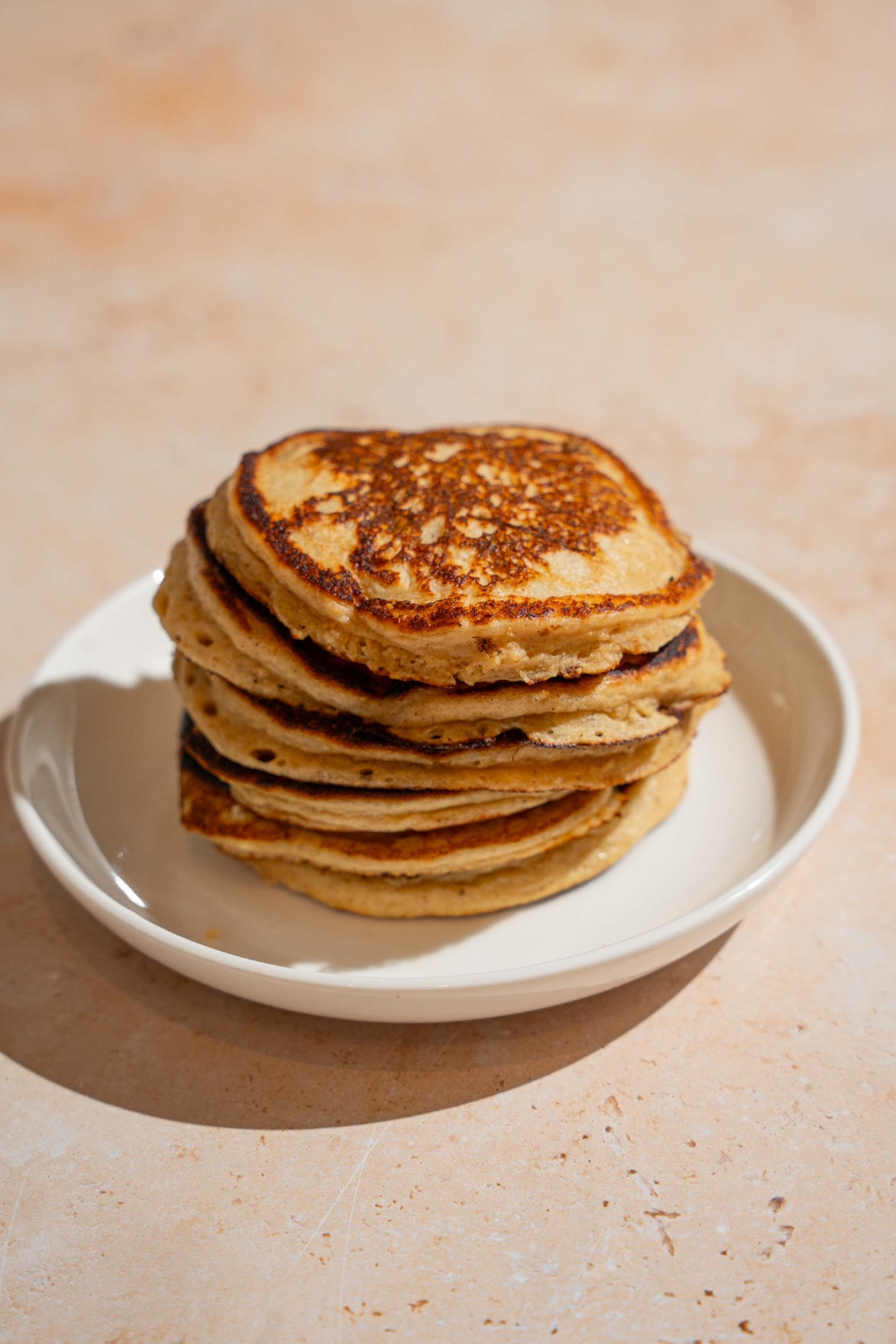 A white plate with a stack of cottage cheese banana pancakes. The plate is on a tan counter.