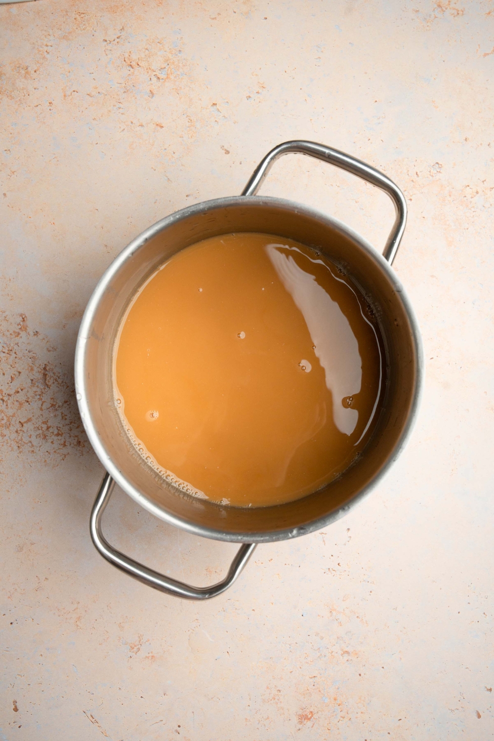 A stock pot with simmering oyster sauce. The pot is on a tan counter.