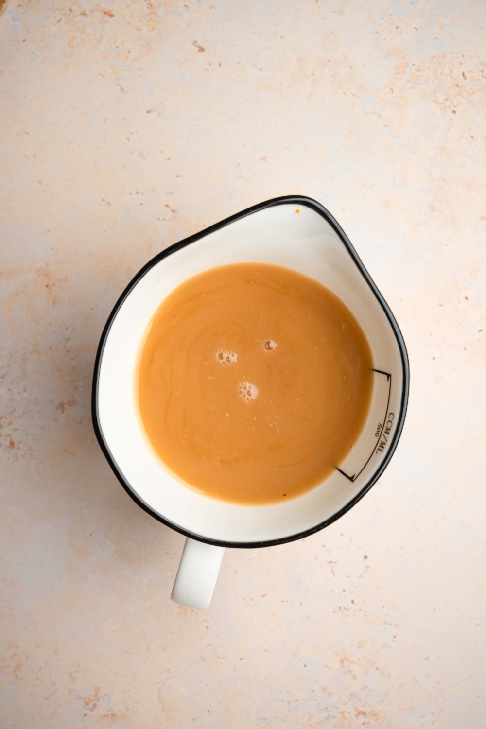 A ceramic pitcher with strained oyster sauce. The pitcher is on a tan counter.