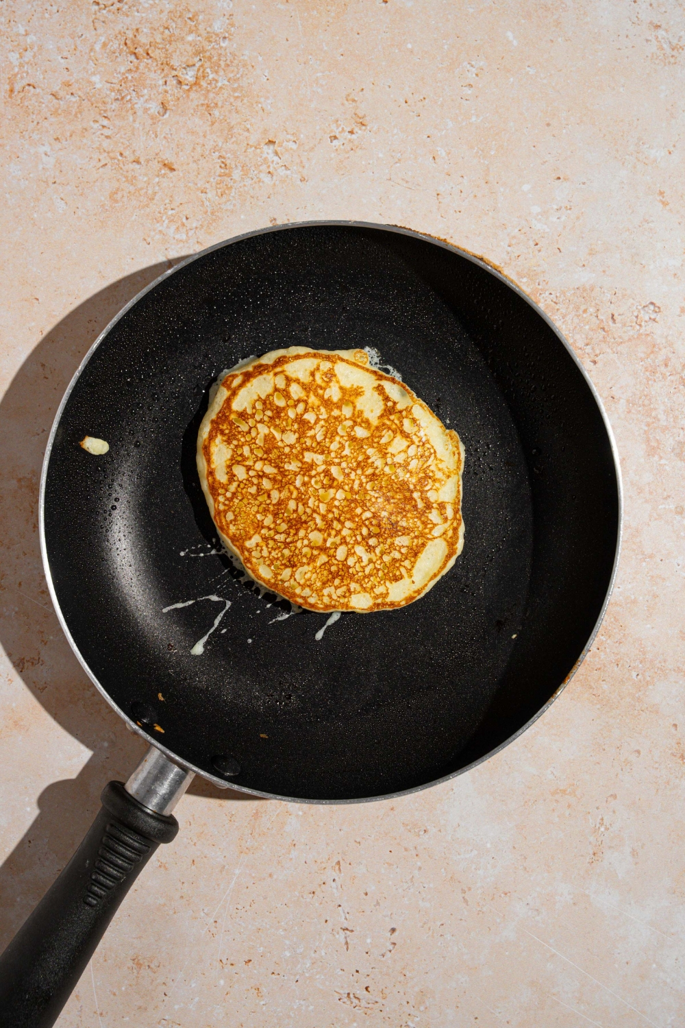 A skillet with a cooked pancake. The skillet is on a tan counter.