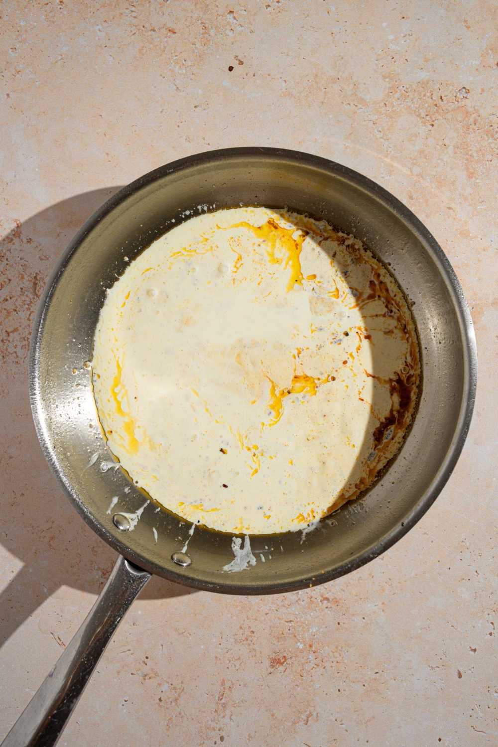 A skillet with alfredo sauce. The skillet is on a tan counter.