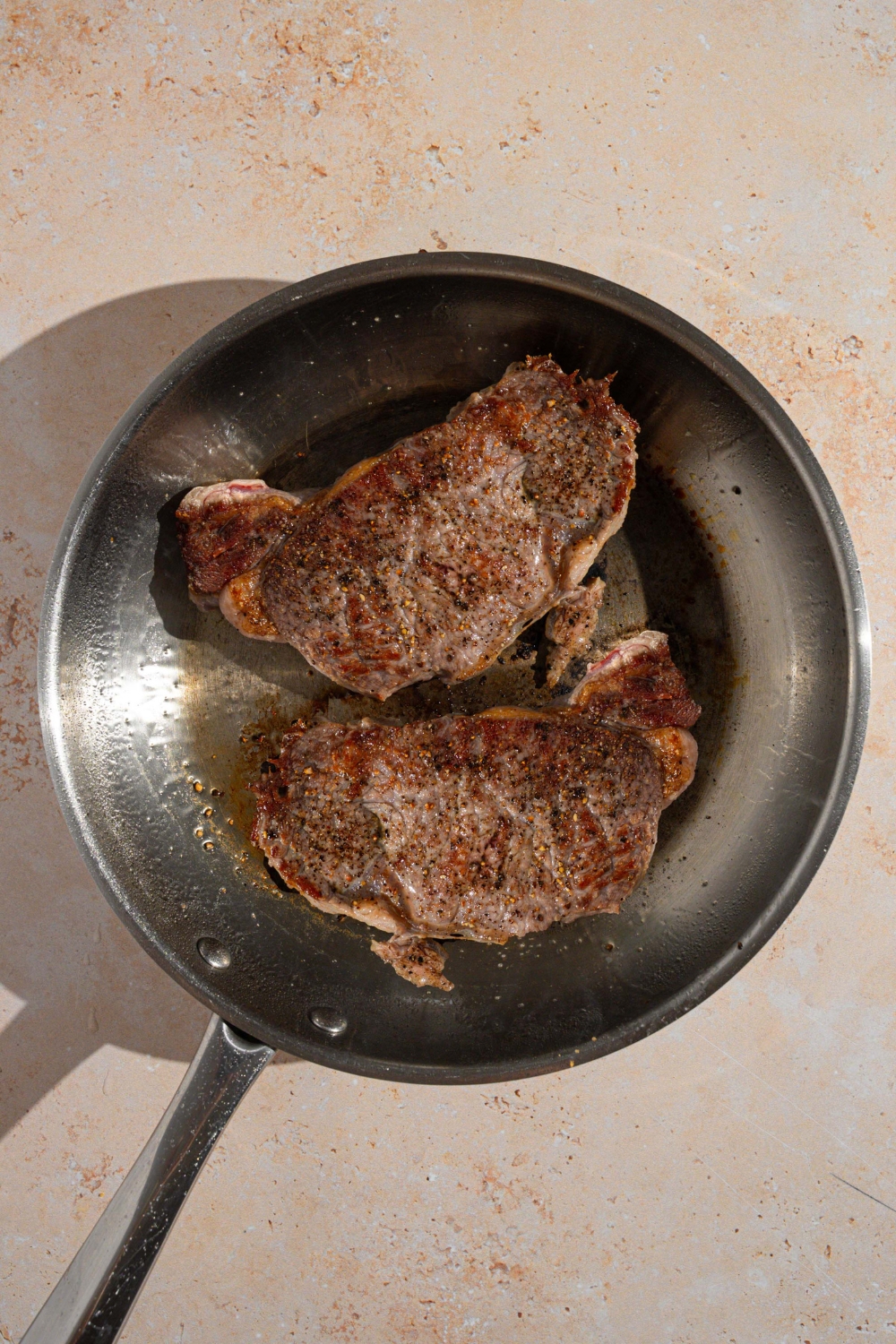 A skillet with two steaks cooking in butter. The skillet is on a tan counter.