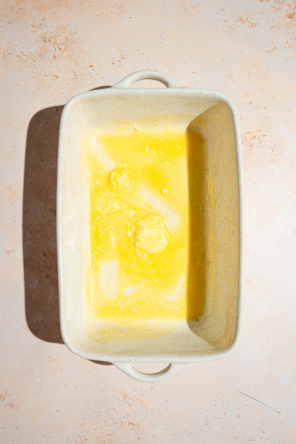 A baking dish with melted butter coated on the bottom. The dish is on a tan counter.