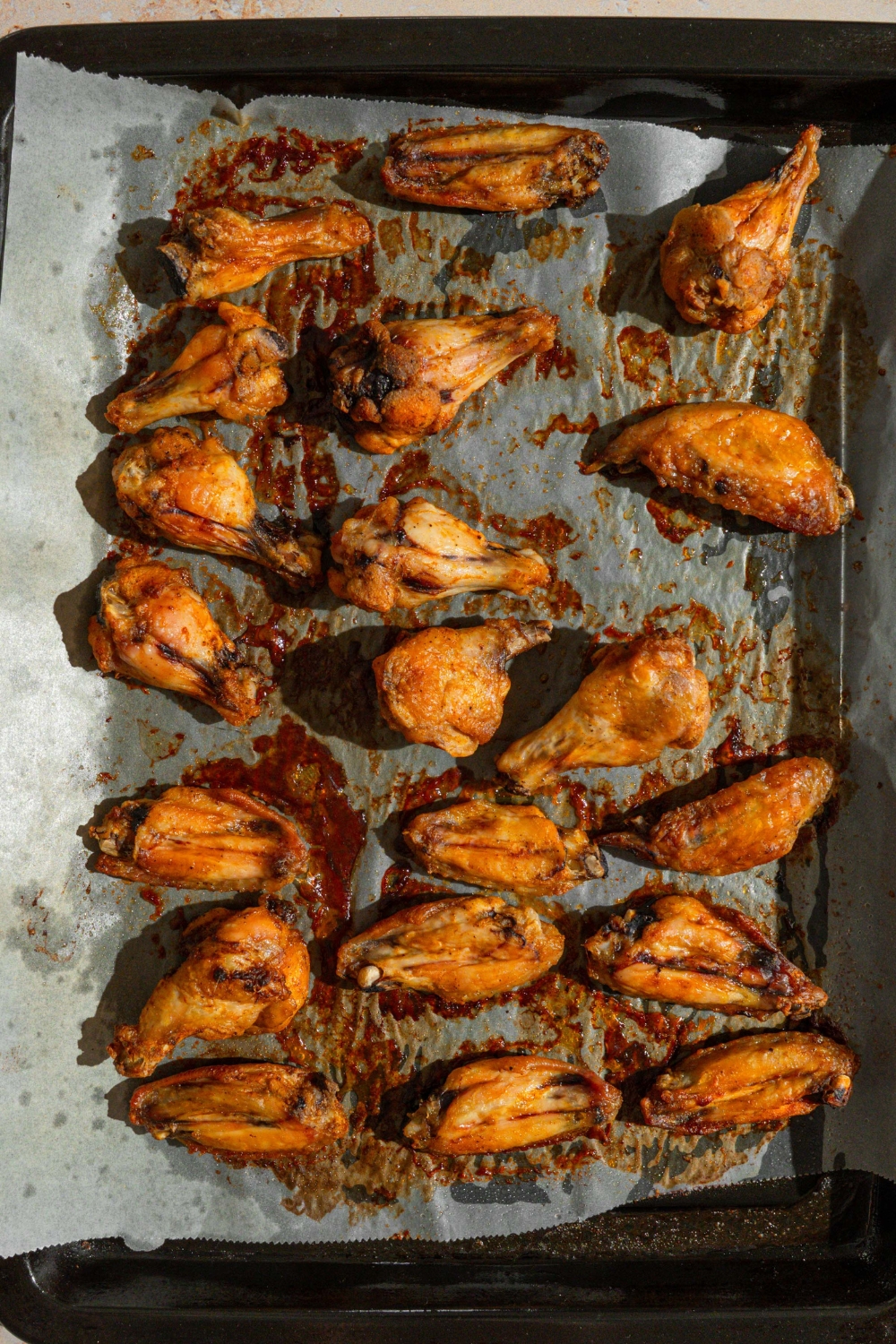 A baking sheet lined with parchment paper with several wings baked in Louisiana rub.