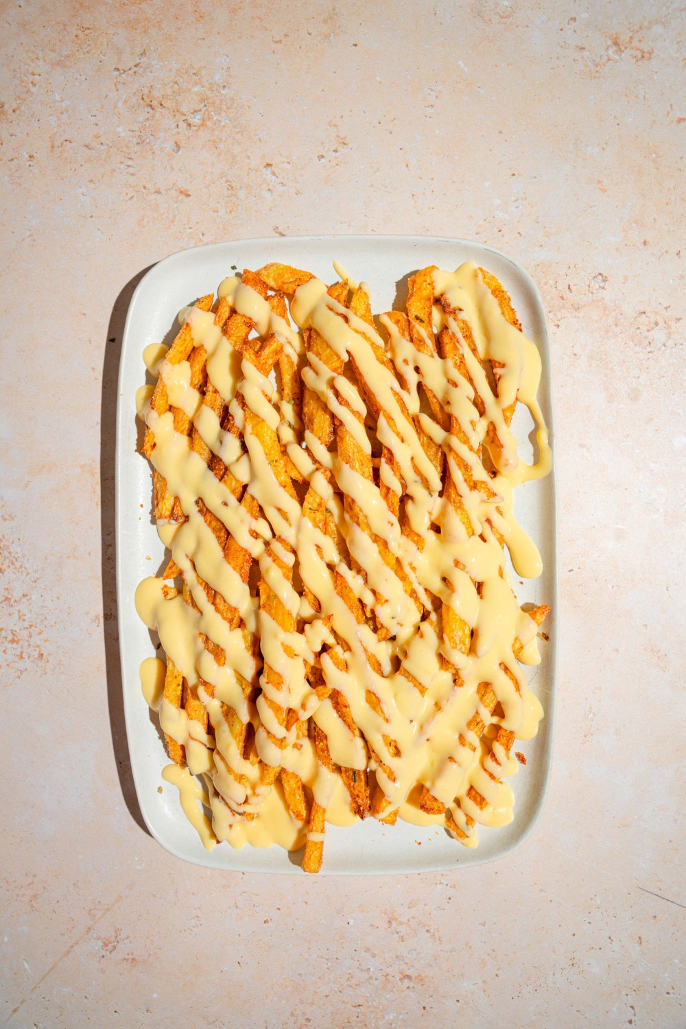 A white platter with copycat Wingstop Voodoo fries drizzled with cheese. The platter is on a tan counter.