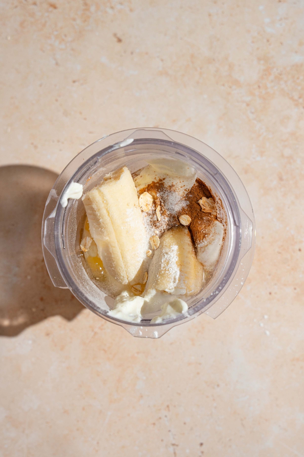 A glass jar with ingredients to make cottage cheese banana pancake batter including bananas, cinnamon, oats, and cottage cheese. The jar is on a tan counter.