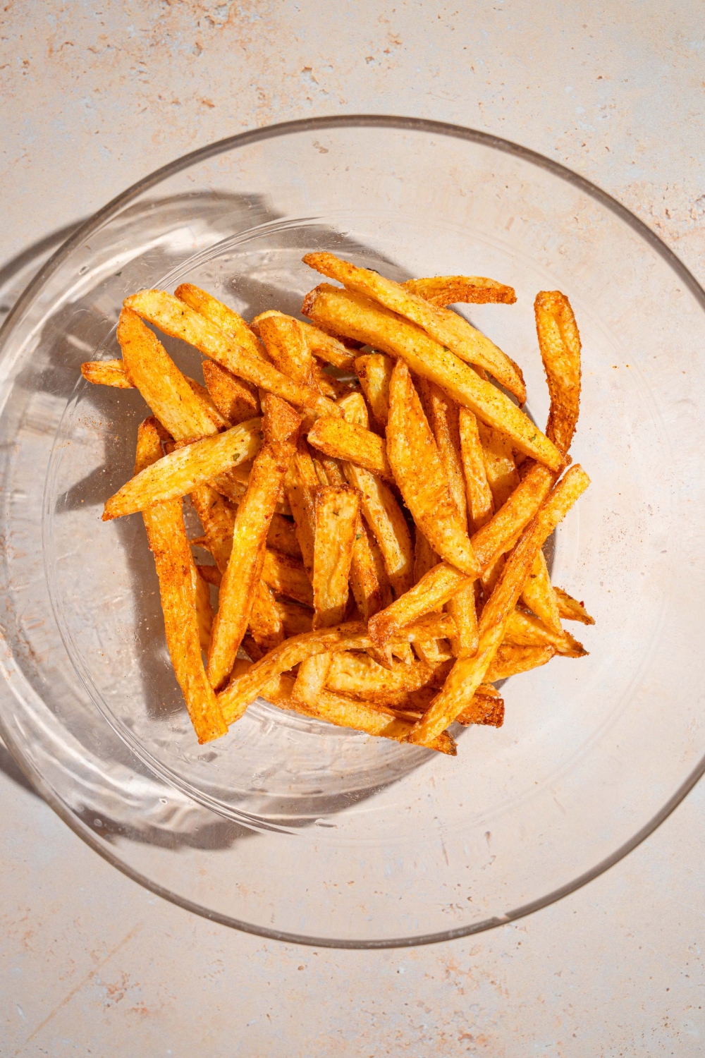 A glass bowl with french fries tossed in cajun seasoning. The bowl is on a tan counter.