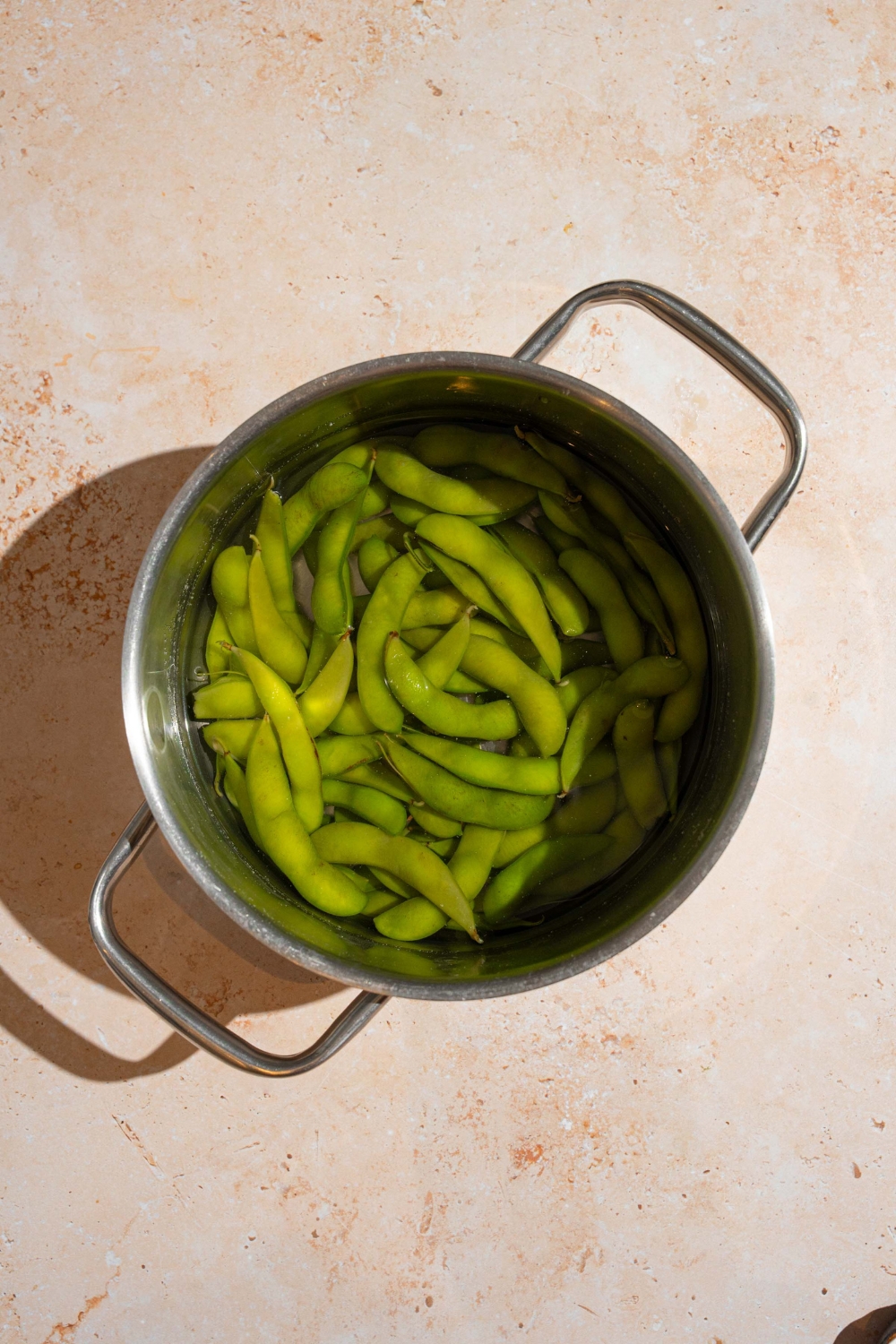 A pot with frozen edamame cooking in water. The pot is on a tan counter.