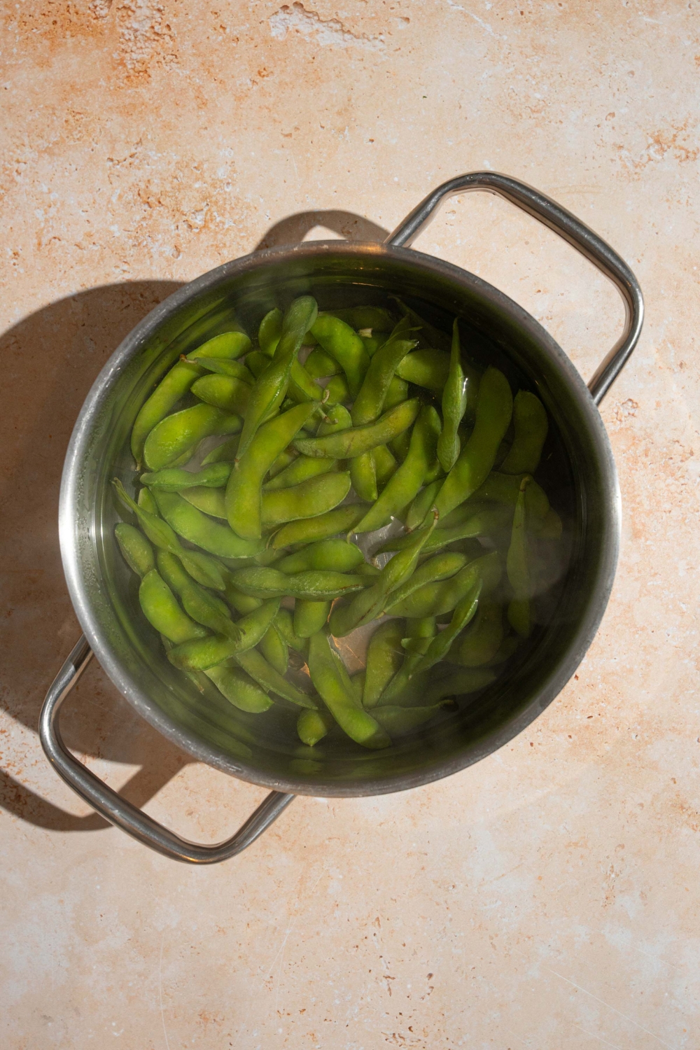 A pot with frozen edamame cooking in water. The pot is on a tan counter.