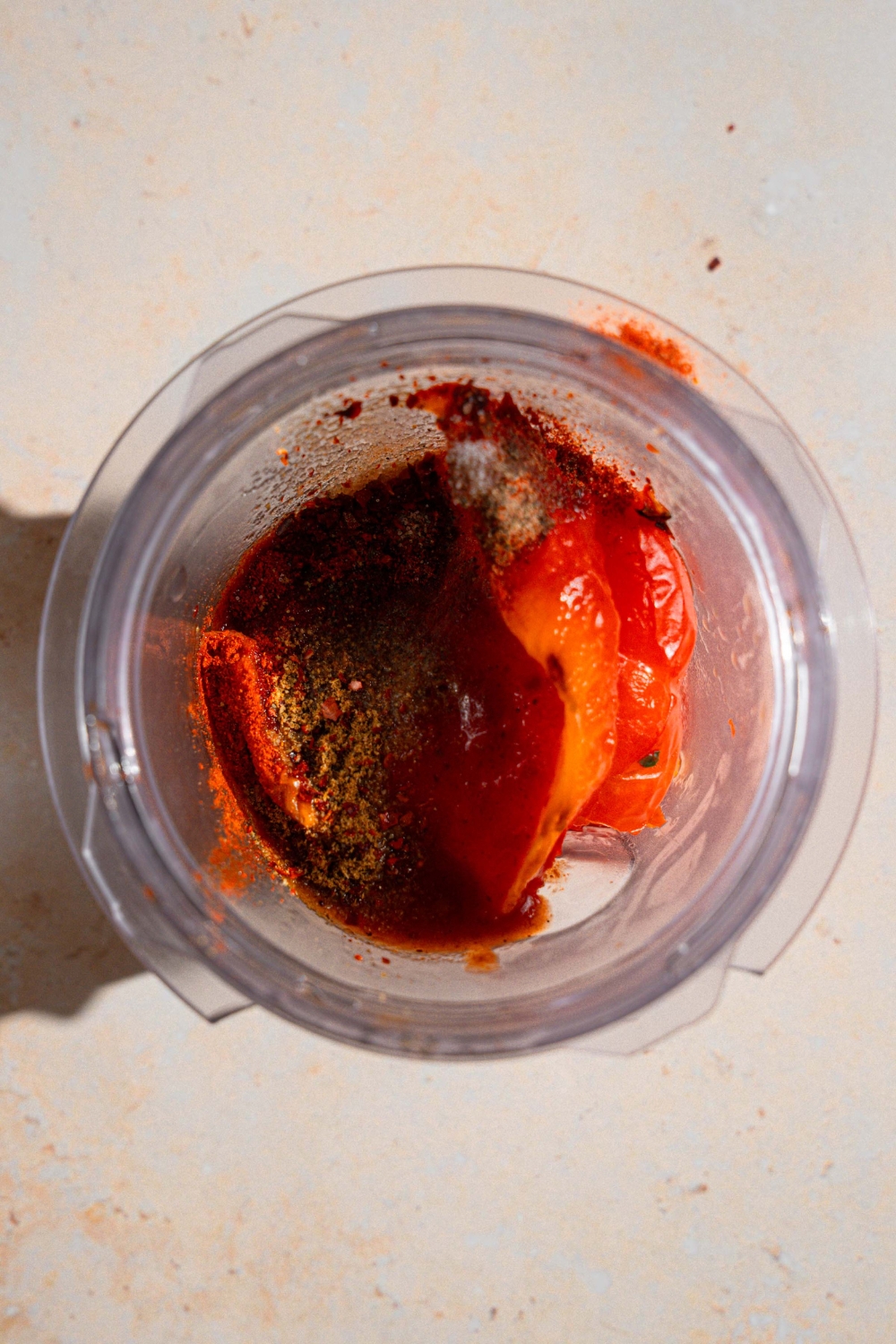 A blender with roasted peppers and other ingredients to make chimichurri sauce. The blender is on a tan counter.