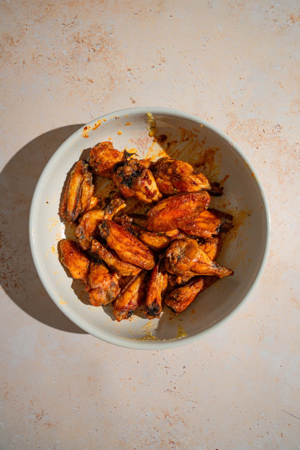 A bowl of baked wings tossed in Wingstop Louisiana rub. The bowl is on a tan counter.