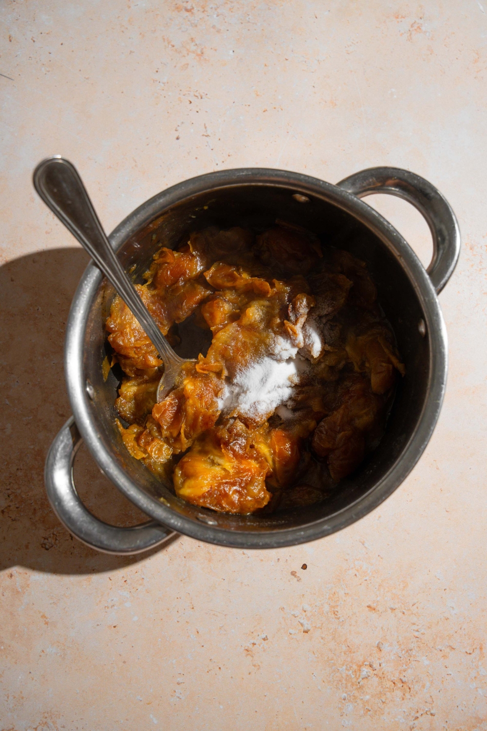 A pot with a spoon mixing date filling with baking powder. The pot is on a tan counter.