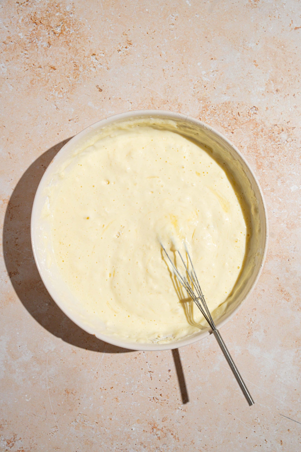 A white bowl with a whisk mixing small batch pancake batter. The bowl is on a tan counter.