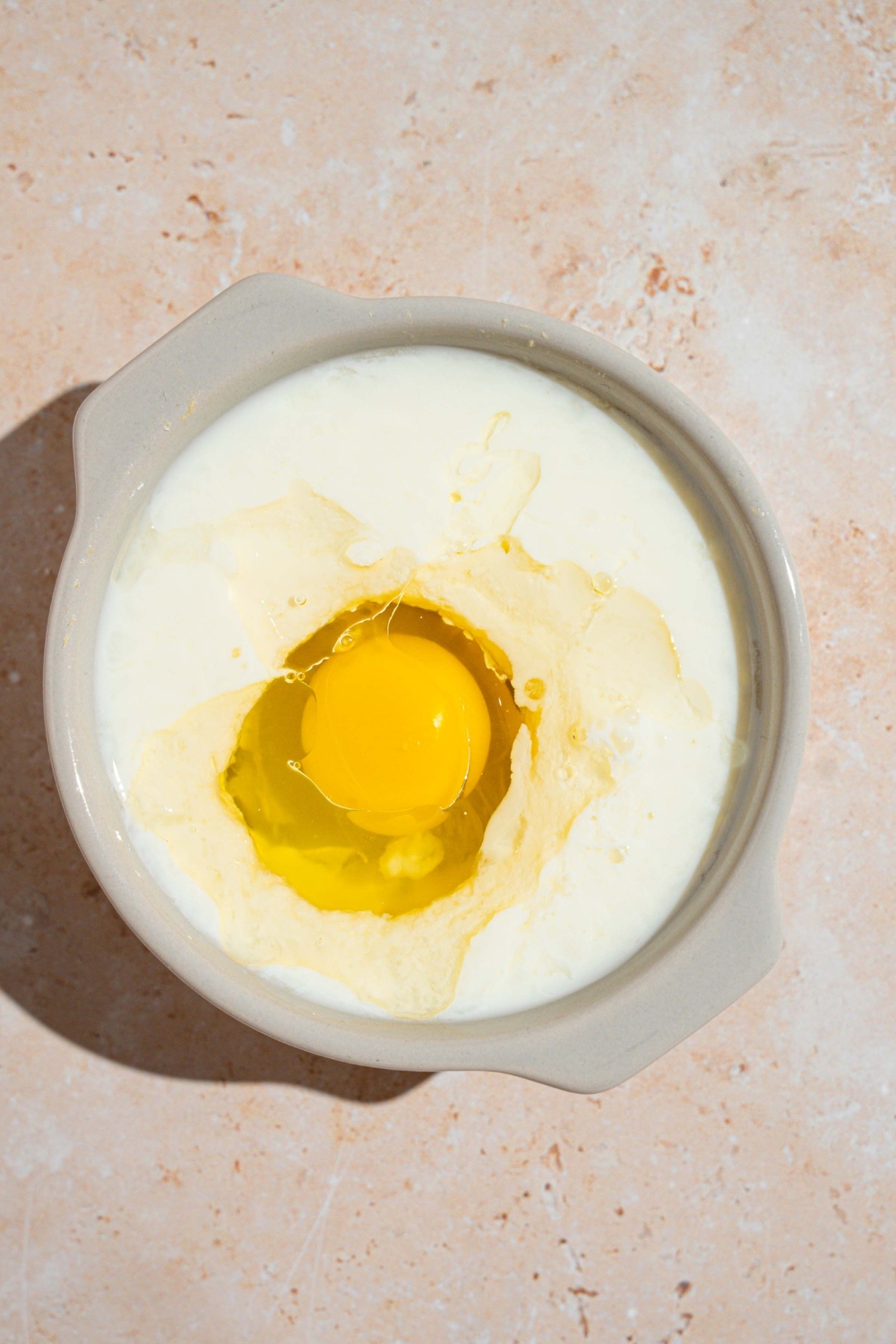 A large white bowl with wet ingredients to make pancake batter including buttermilk, oil, and egg. The bowl is on a tan counter.
