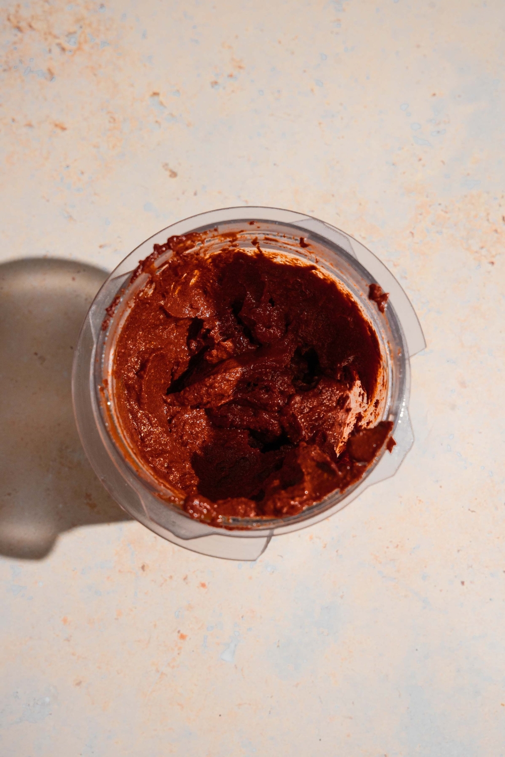 A blender jar with blended adobo sauce. The jar is on a tan counter.