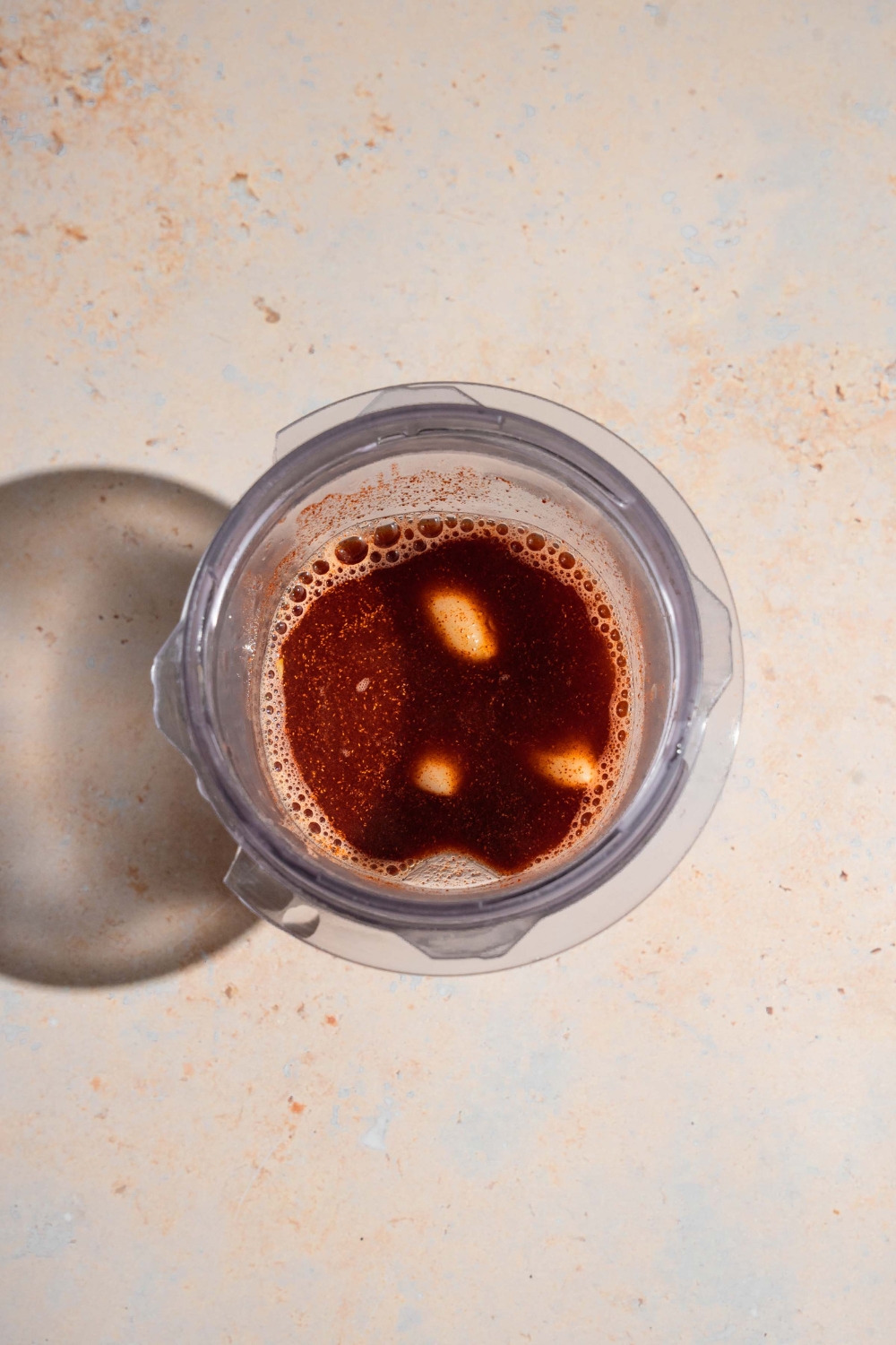 A blender jar with adobo spices mixed with garlic and vinegar. The jar is on a tan counter.