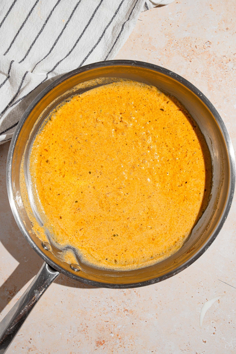 A skillet with cooked cajun alfredo sauce. The skillet is on a tan counter with a white striped napkin.