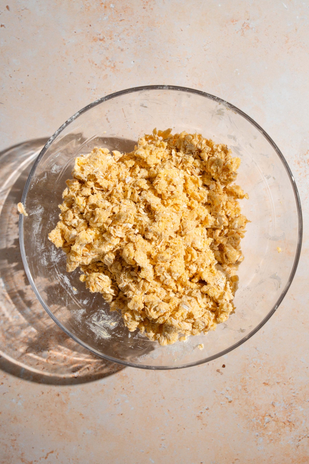 A glass bowl with ingredients to make old fashioned date bar crust mixed with butter. The bowl is on a tan counter.