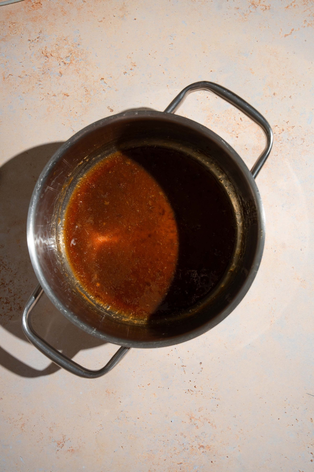 A stock pot with cooked oyster sauce. The pot is on a tan counter.