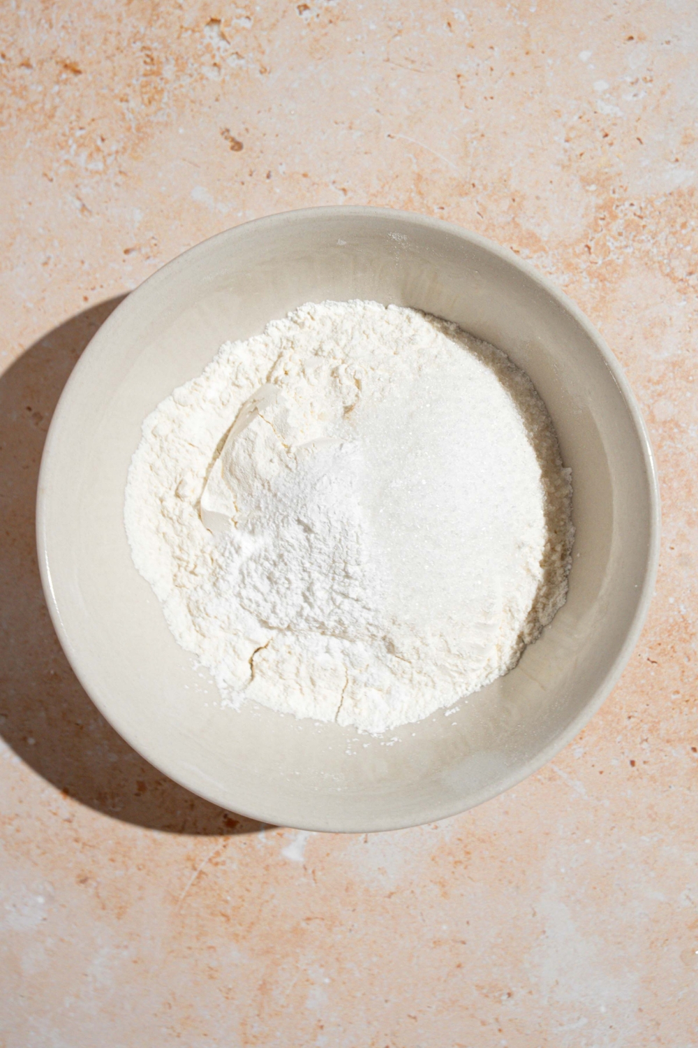 A white bowl with dry ingredients to make small batch pancakes including flour, baking soda, baking powder, salt, and sugar. The bowl is on a tan counter.