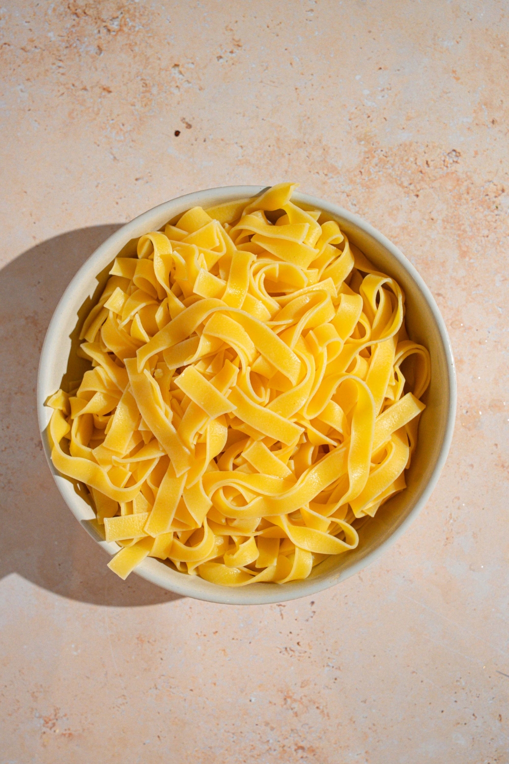 A bowl of cooked fettuccine pasta. The bowl is on a tan counter.